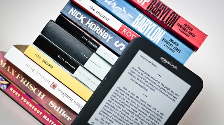 A stack of books sitting behind a Kindle