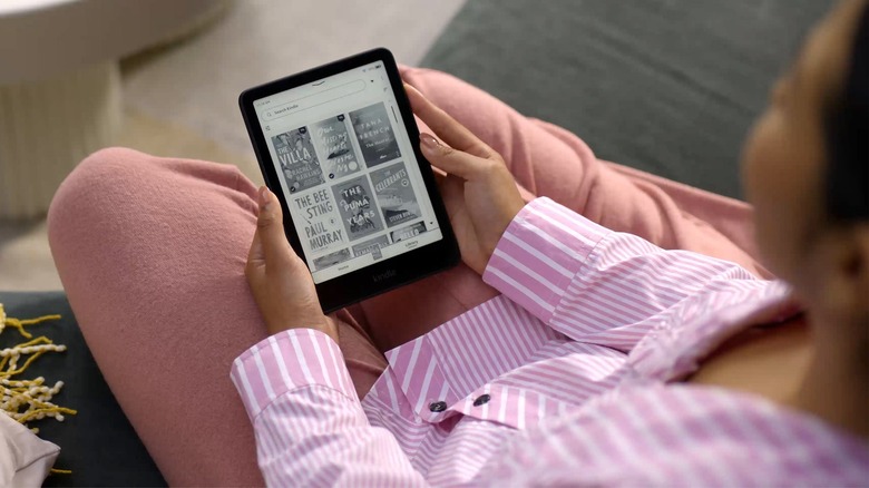 Woman sitting while holding a Kindle showing the library page