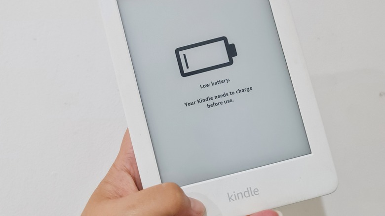 A hand holding a white Kindle showing a low battery screen