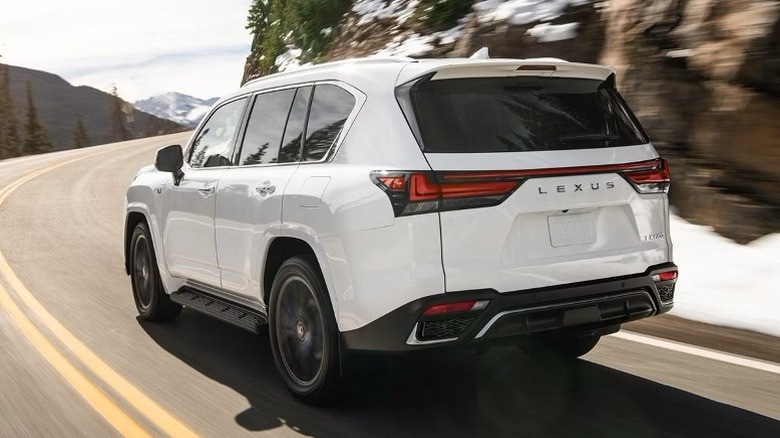 White Lexus LX driving around a turn on a road between mountains