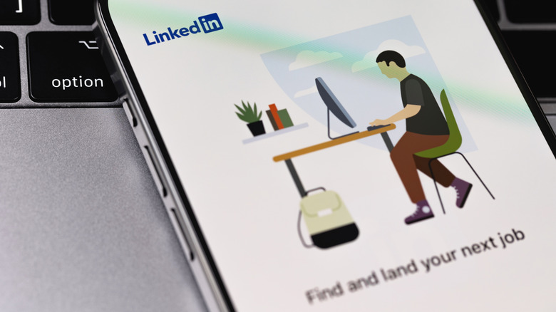 Smartphone next to a computer keyboard showing LinkedIn screen and the text "Find and land your next job"