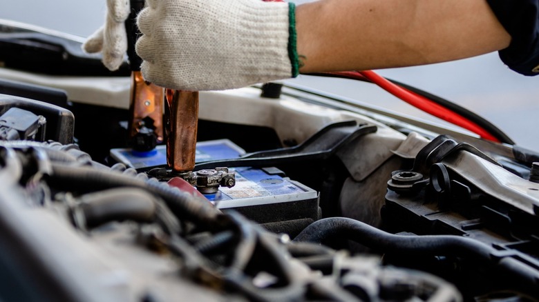 Hands holding jumper cables on car battery