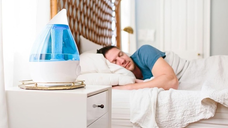 Person sleeping with a 1 Gal. Drop Ultrasonic Cool Mist Humidifier on the nightstand.