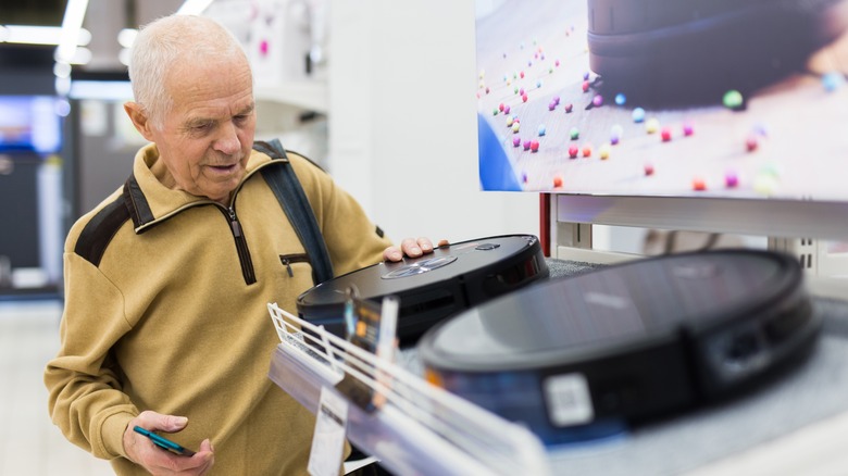 An elderly man browsing robovacs in a store.