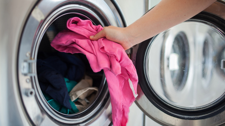 A person loading a pink garment into a washer