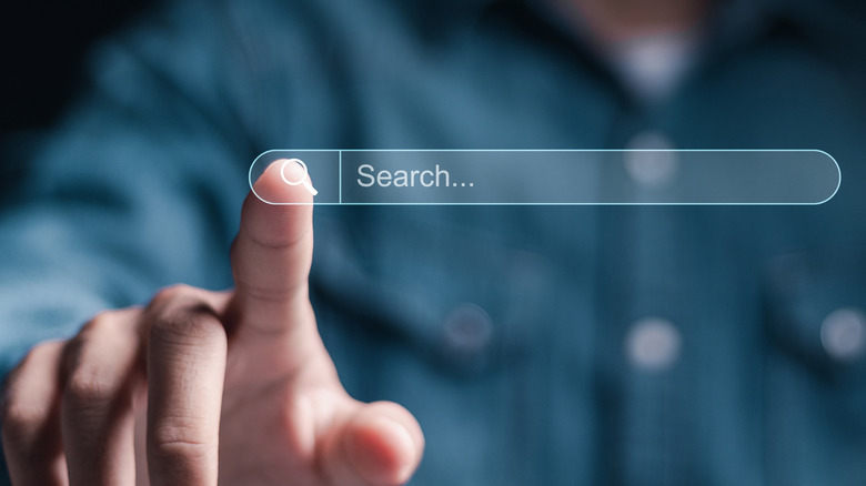 A blurred figure in a blue shirt is shown in the background with their finger - which is in focus - pointing to the front of the image. A seach bar is superimposed on the image and the finger is about to click the search icon.