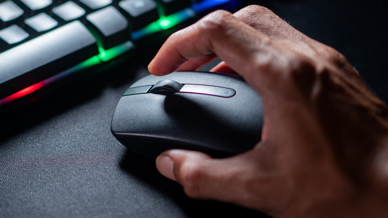 Close up of a hand using computer mouse next to RGB keyboard