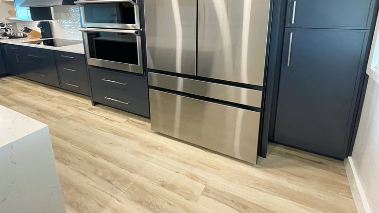 Close-up of upscale kitchen appliances in a modern coastal home. The stainless steel appliances features a double wall oven and sleek refrigerator. Plus, an oversized blue hood with electric cooktop.