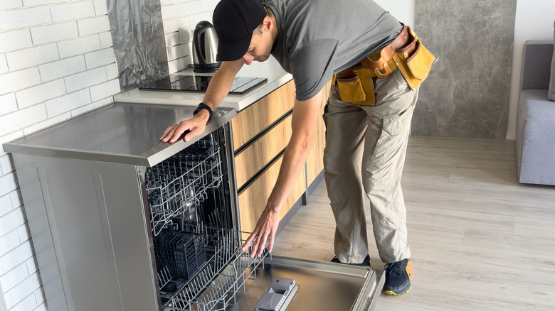 Young Repairman Service Worker Repairing Dishwasher Appliance In Kitchen.