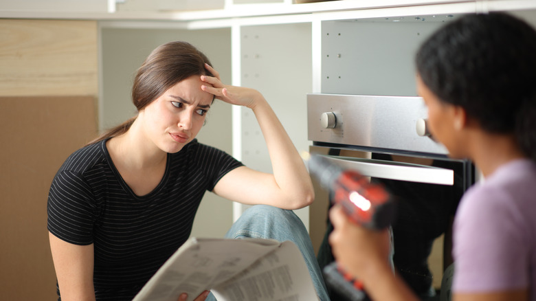 two women trying to install a dishwasher