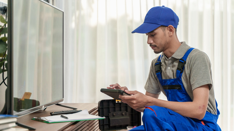 Young Asian man technician checking or setting up television with digital tablet.