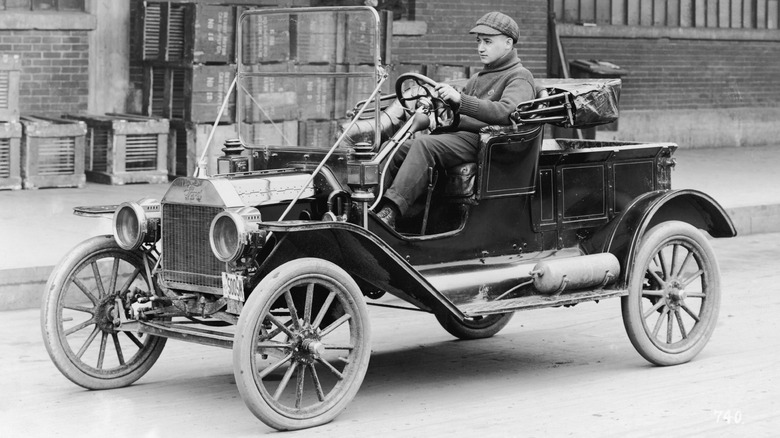 A man wearing a cap and driving a Ford Model T.