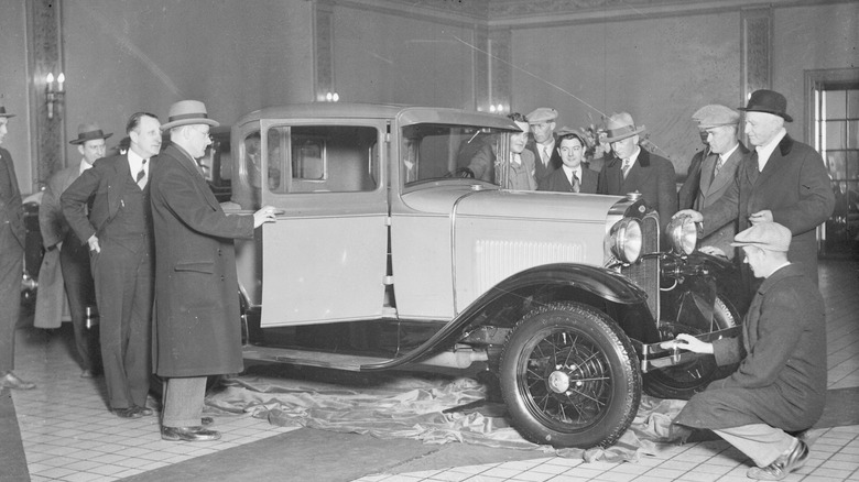 Group of people inspecting new Ford Model A at show, period photograph