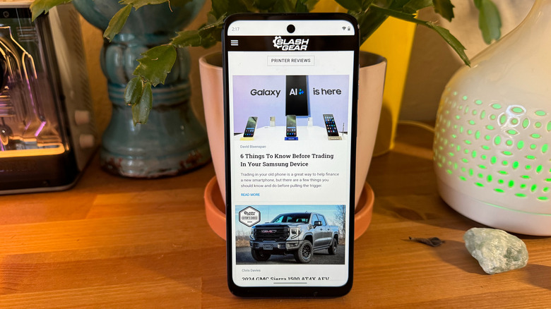 Motorola G Play (2024) on the SlashGear website on a wooden table resting against some potted plants.