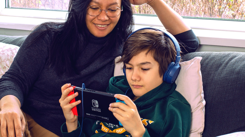 Boy plays on Nintendo Switch while mother watches overhead.