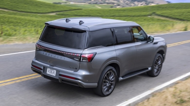 2025 Infiniti QX80 driving on a road next to lush green field