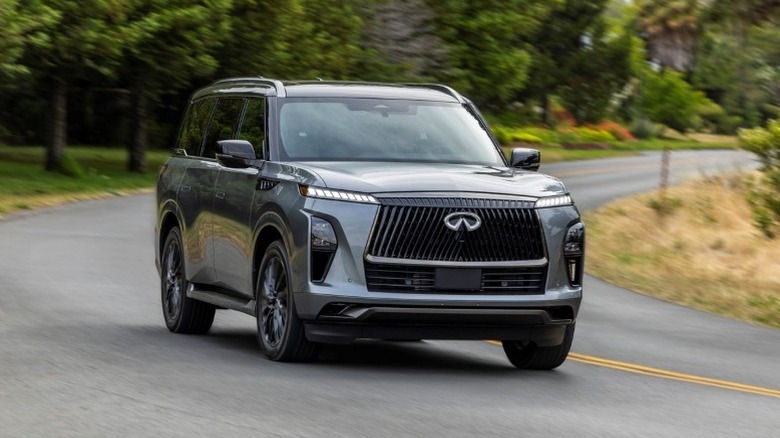 Side profile of a 2025 Infiniti QX80 driving around a curve with trees in the background