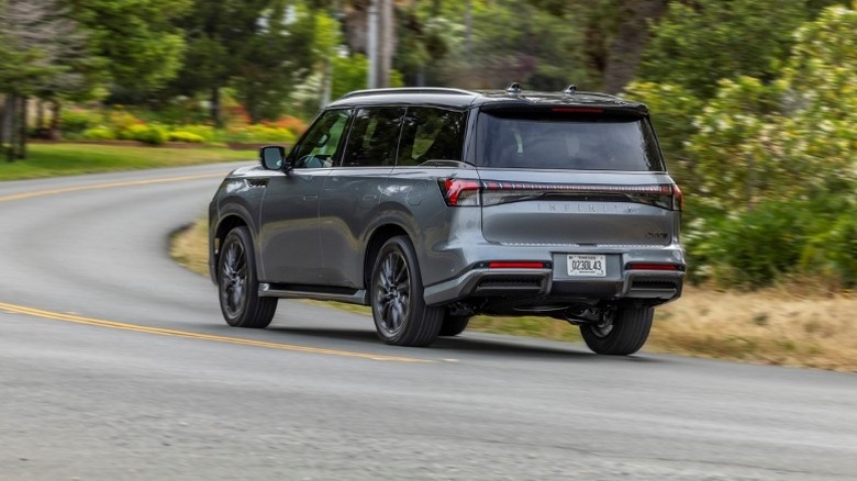 Infiniti QX80 driving around a curve with trees in the background