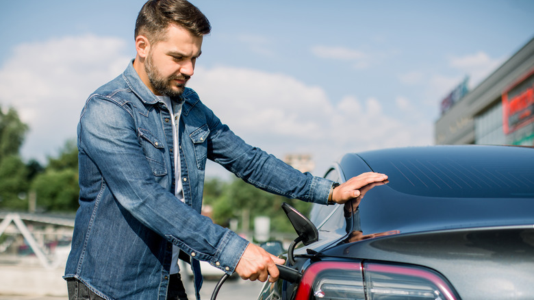 Man squinting while charging EV at station