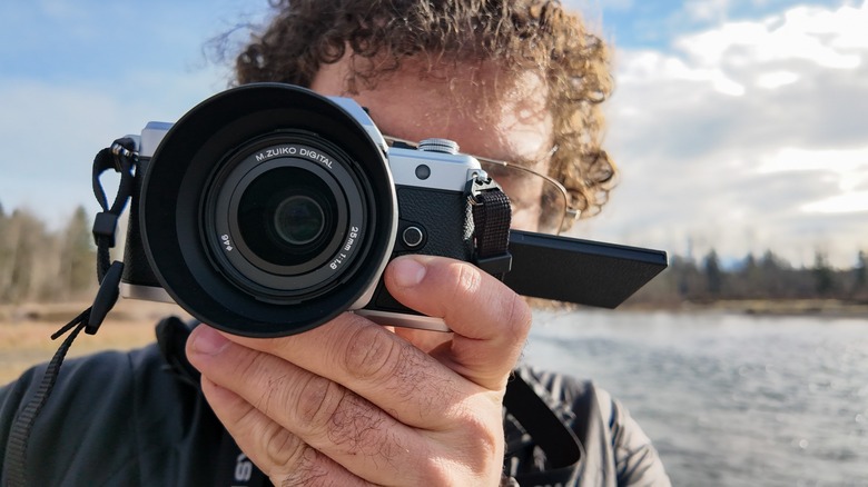 A man taking a photo with the OM System OM-3 next to a river.