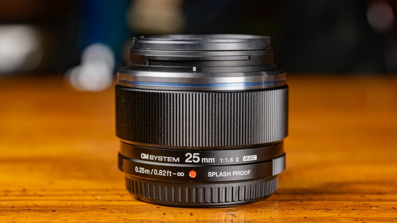 The M.ZUIKO Digital ED 25mm f/1.8 II lens on a wooden table.