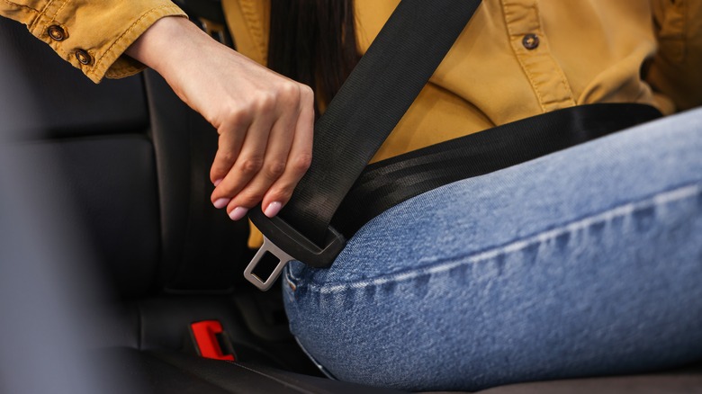 Woman putting on seat belt in a car