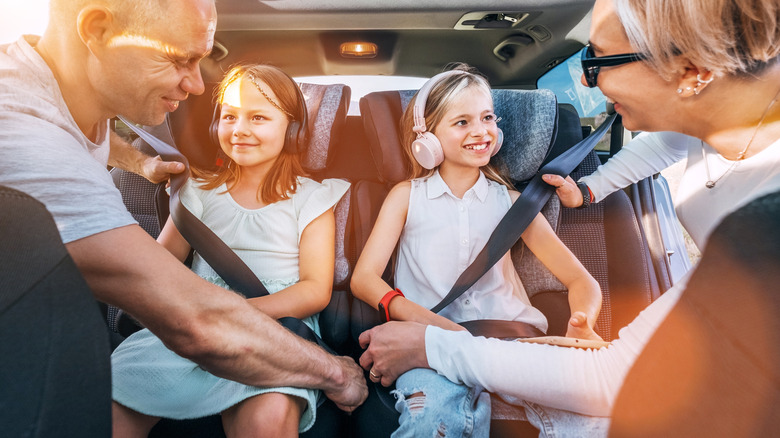 Parents strapping two young girls into their car seats