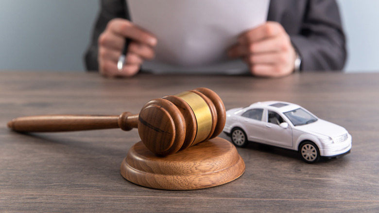 A gavel next to a toy car on a table with a man in the background