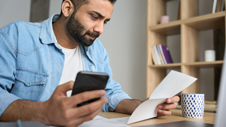 man holding phone and paper