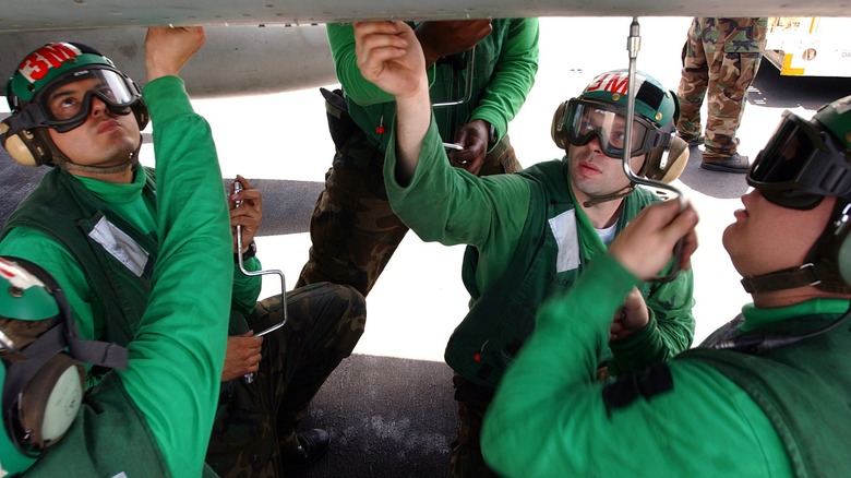 Green shirts performing maintenance on an F/A-18 Hornet