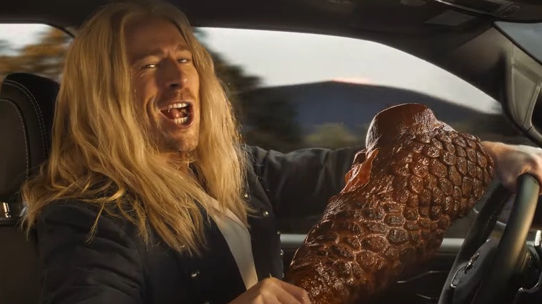 Glen Powell eating a smoked dragon drumstick while driving a Ram truck.