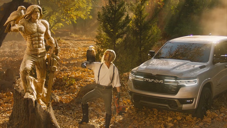 Glen Powell posing next to a chainsaw carving in his likeness and a 2025 Ram 1500 Ramcharger.