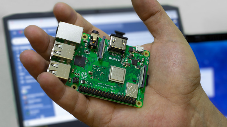 Hand holding Raspberry Pi board with laptop monitor in the background