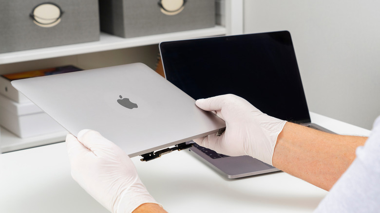 A repair expert fixing an old MacBook laptop.