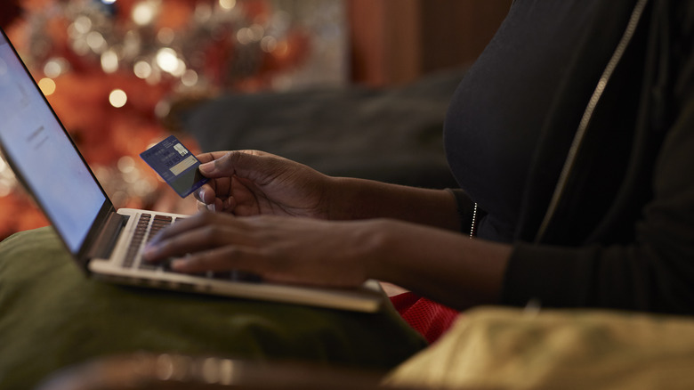 A woman with a laptop on her lap holding a credit card ready to buy