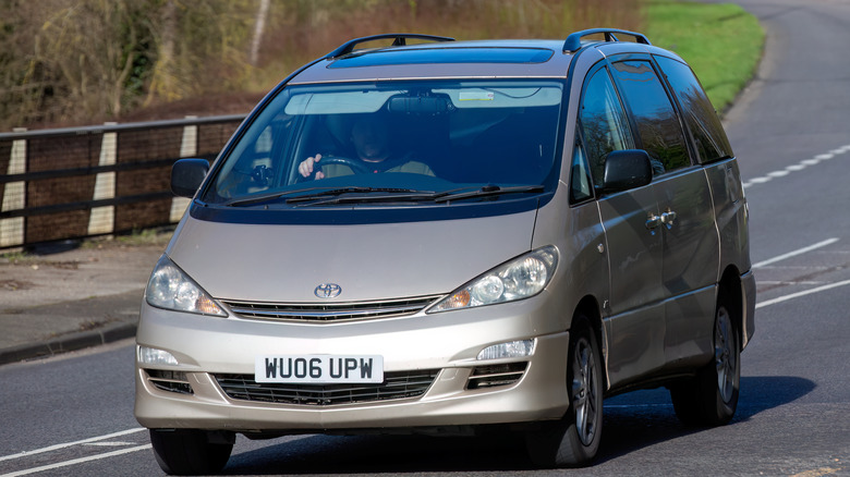 A brown/bronze Toyota Previa being driven by a male driver visible through the windshield