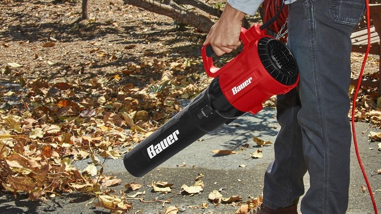 Man pointing Bauer blower towards leaves on pavement