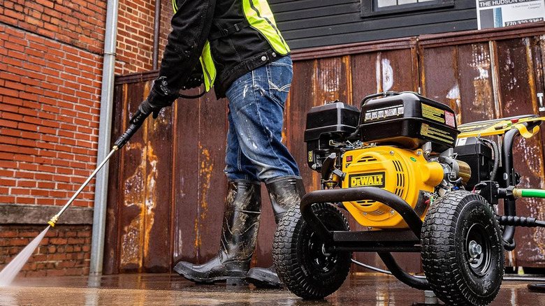 man with high boots hosing down area with DeWalt pressure washer