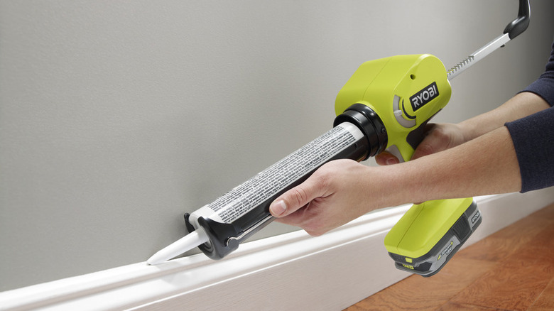 person using Ryobi caulk gun on baseboard