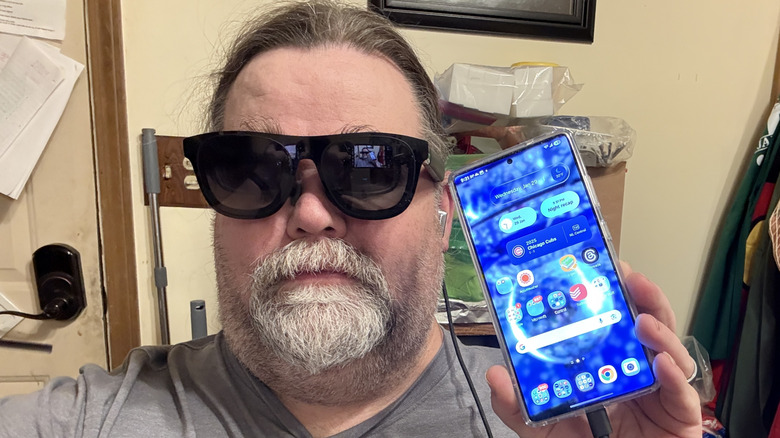 Man wearing AR glasses and holding a Samsung Galaxy S25 Ultra