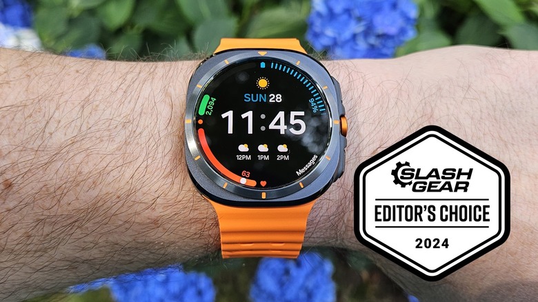 Samsung Galaxy Watch Ultra worn on a wrist in front of a green bush with blue flowers