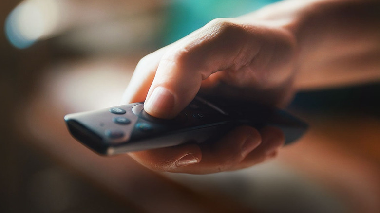 A person's hand pressing a button on black TV remote