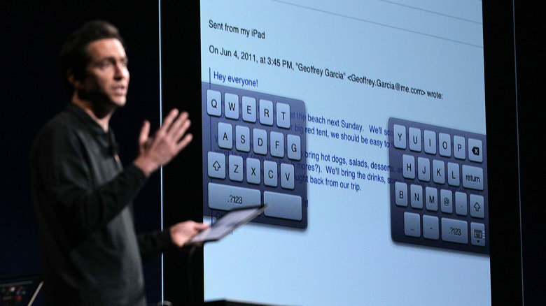 A man standing next to a big screen displaying the iPad split keyboard