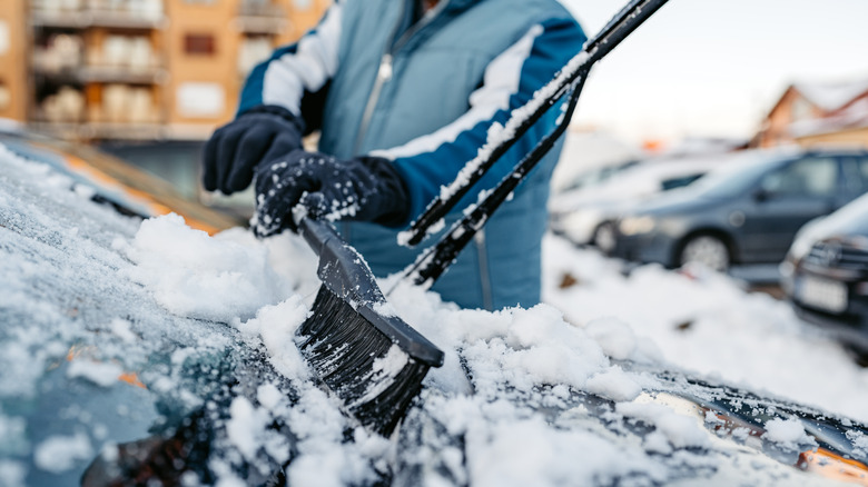 A man brushes off snow from the windshield and wipers