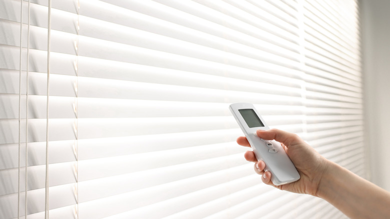 A person using a remote to open a window's blinds.