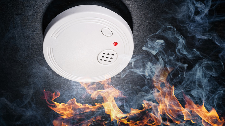 A red light blares from a smoke detector above a raging fire