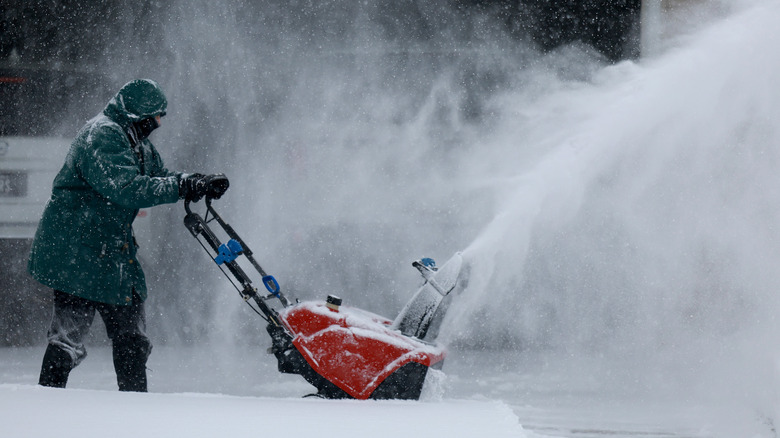 Woman Using Snow Blower To Clear Driveway