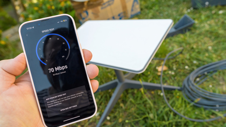 Hand holding phone showing Starlink speed test with Starlink dish in the background