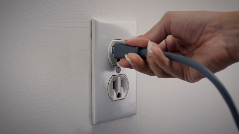 Hand plugging in power supply to wall outlet