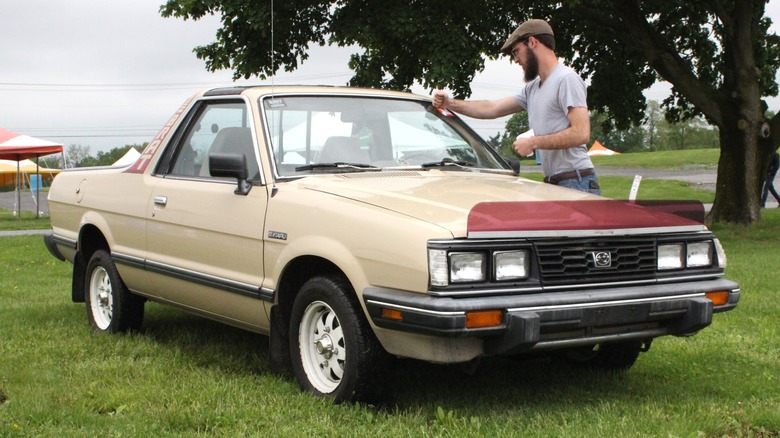 Man with a beige Subaru BRAT parked on grass